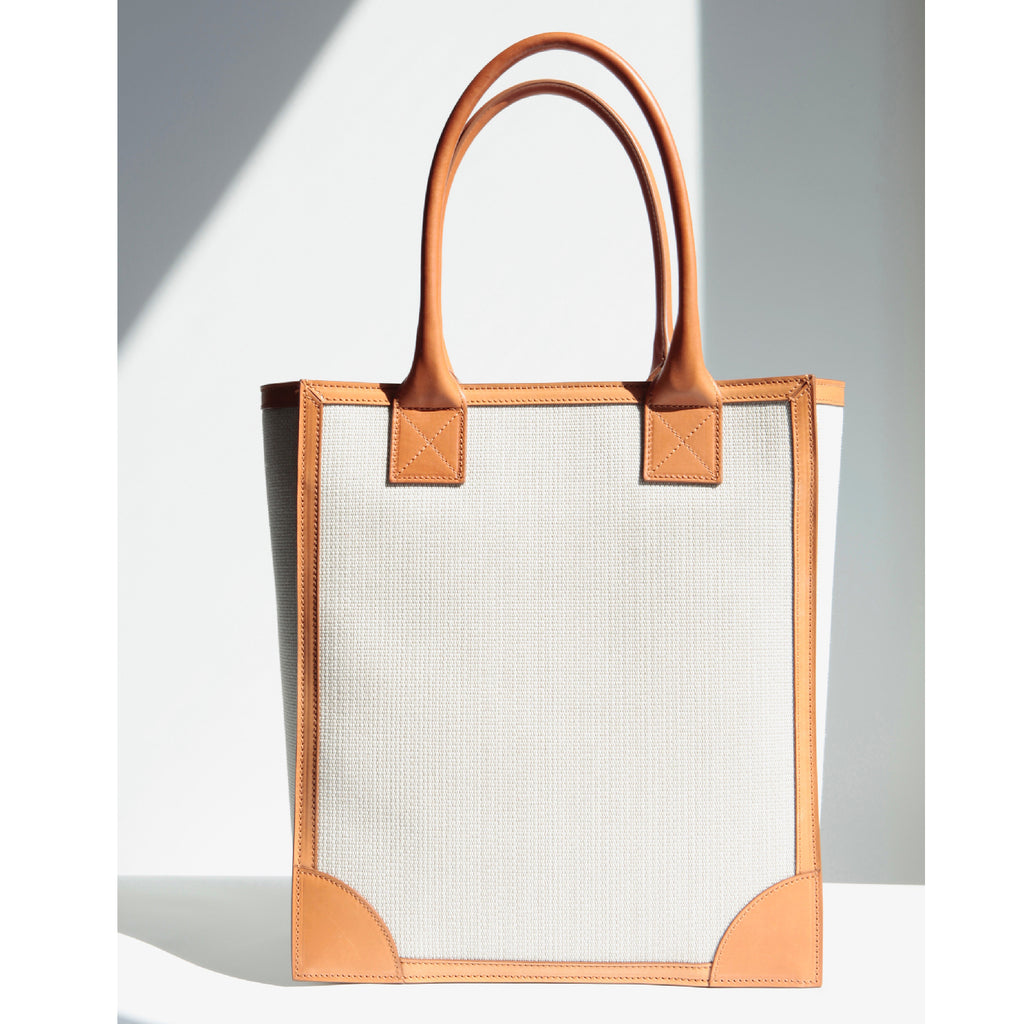 Vertical shopper tote in canvas body with natural veg-tan leather trim around the borders and the long handles. Wear comfortably over the shoulder or carry by the handles. Spacious interior for work essestials. Structured body for the power casual wear.